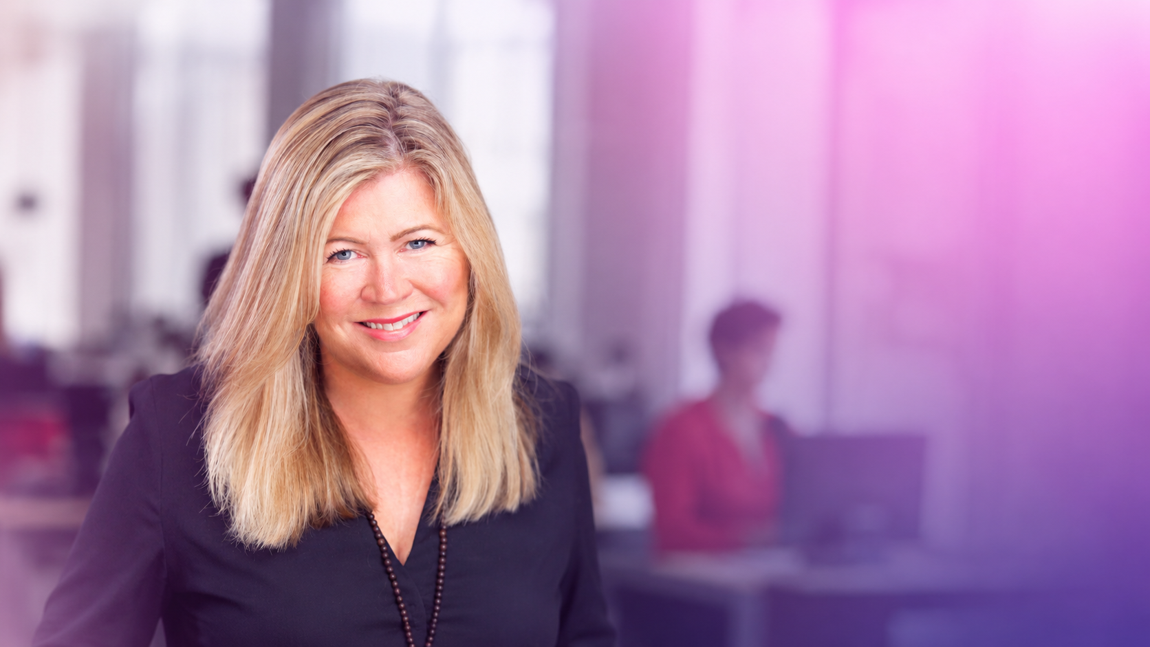 Smiling blonde woman in a black blouse in a modern office setting (head-and-shoulders)